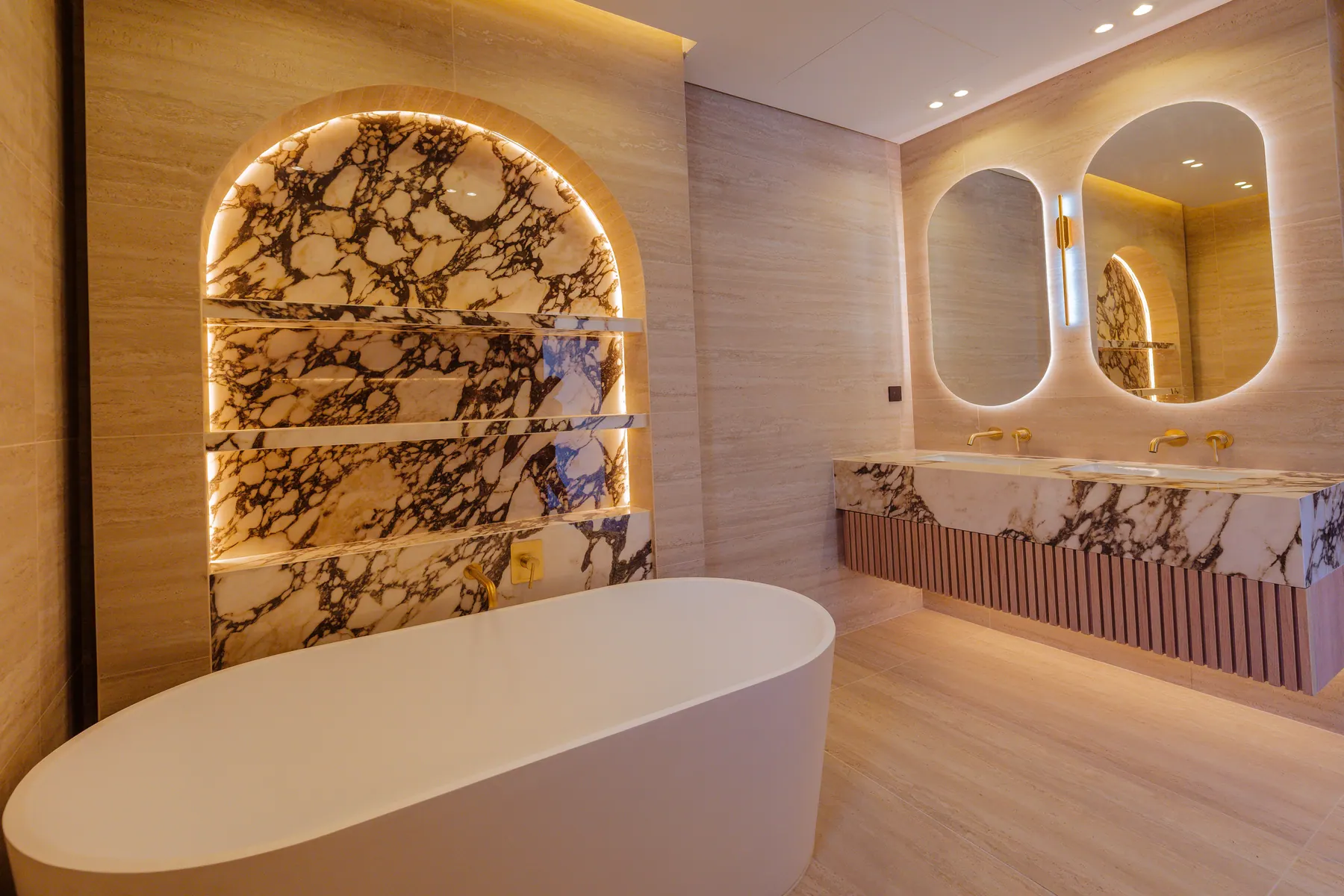 Master bathroom with a viola marble arched niche, freestanding tub and twin oval mirrors