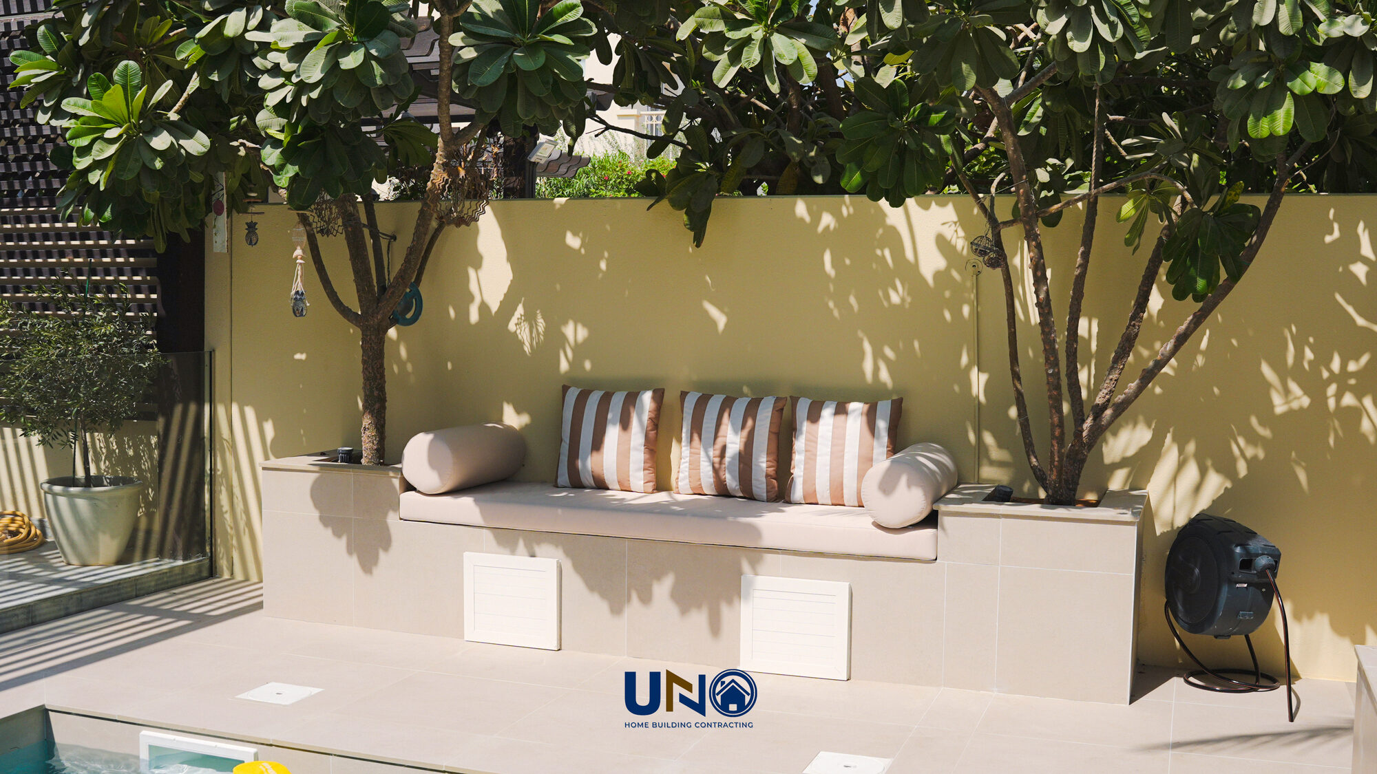 Raised bench seating beside the pool with a shade tree